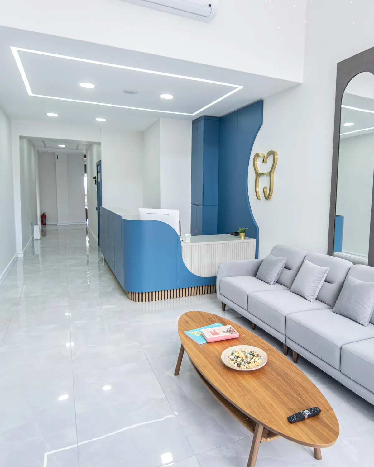 Kliniğin karşılama alanı: mavi resepsiyon bankosu, altın diş logosu ve bekleme koltukları